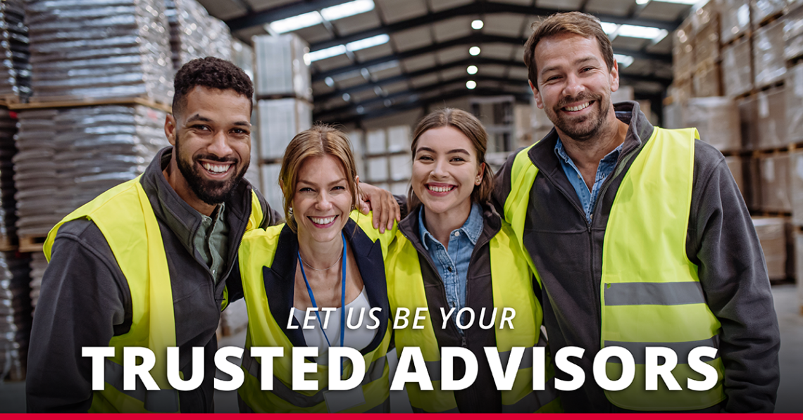 Group of people in warehouse setting embracing and smiling at camera with overlaid text "let us be your trusted advisors"